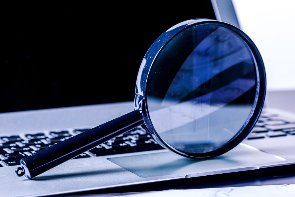Closeup of round, hand-held magnifying glass propped on its circular edge and handle on the trackpad of a laptop.