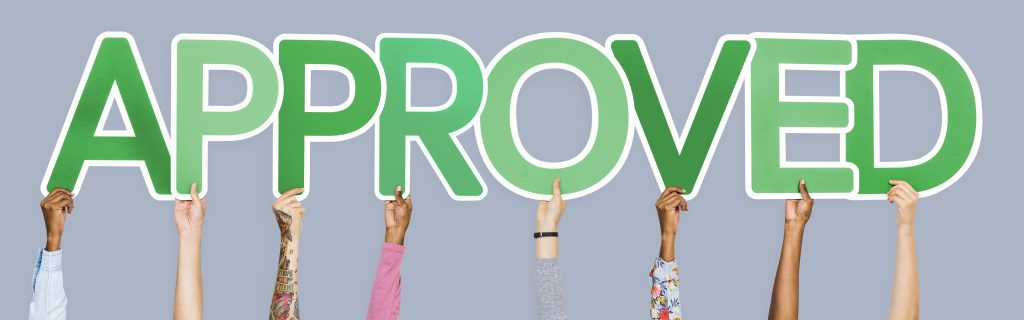 Hands holding up green letters that form the word approved.