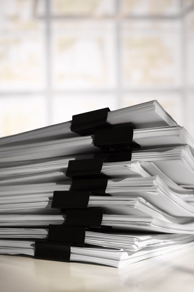 Stack of documents using black binder clips as separators between each set.