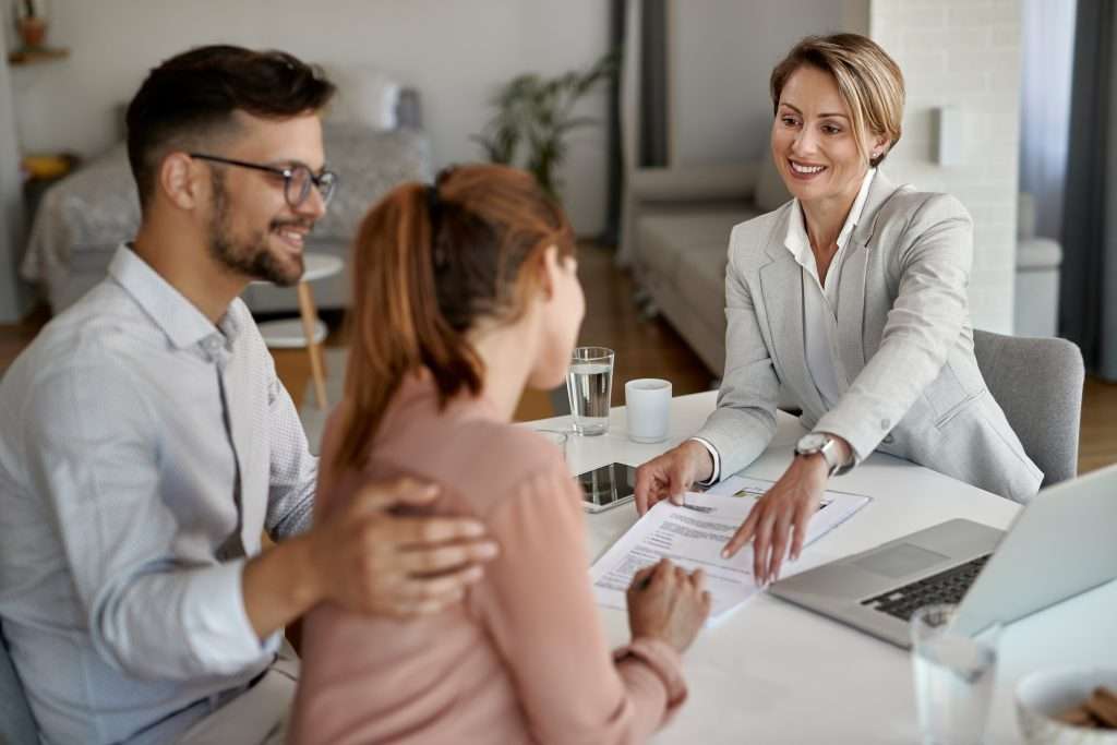 Happy female notary showing young couple where to sign their living trust documents.